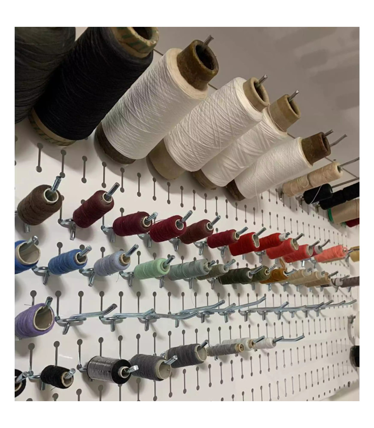 پگ برد حرفه ای با مجموعه ای از رنگ های متنوع نخ در یک دیوار نصب شده. این ابزار برای خیاطی و صنایع دستی ضروری است.